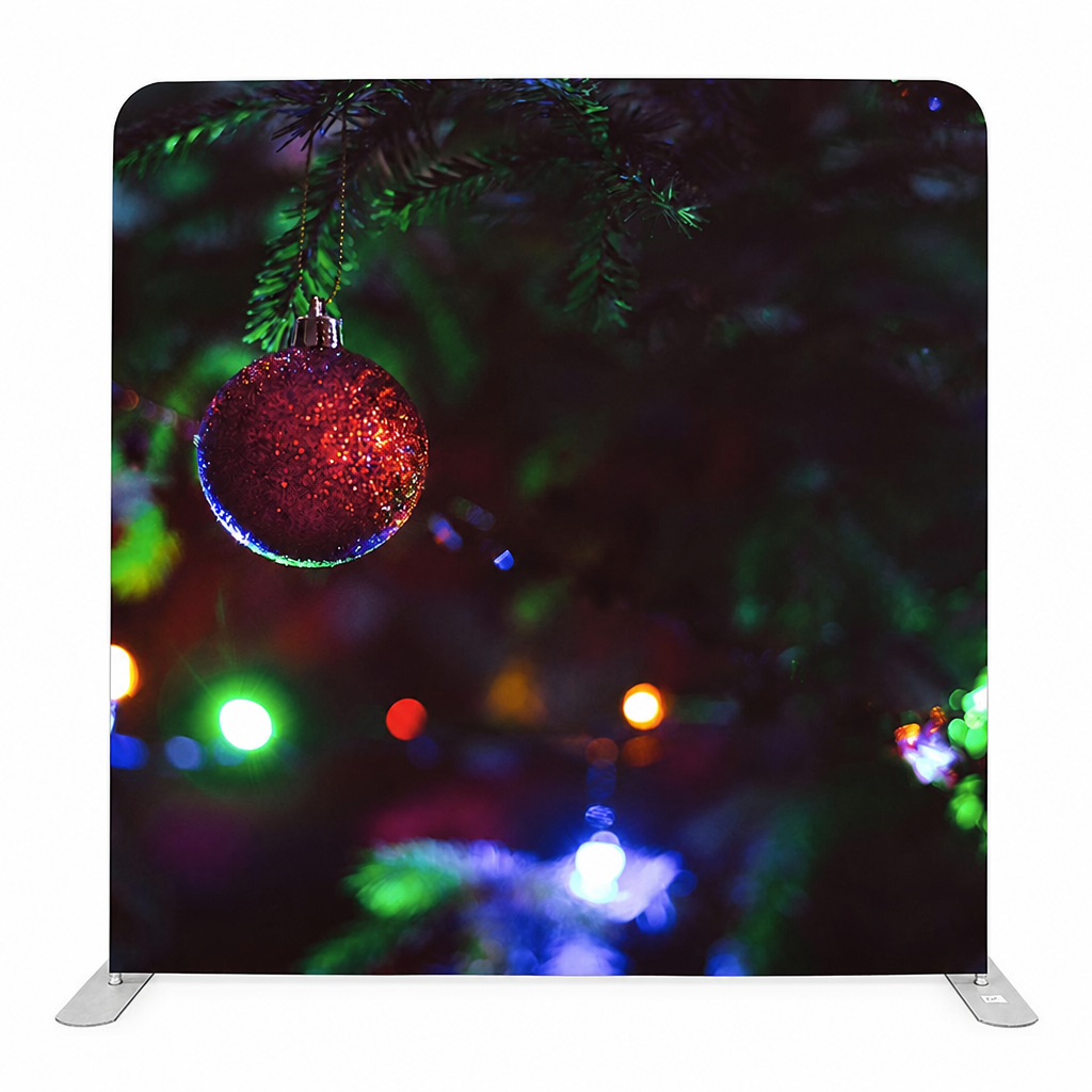 Christmas red ornament close-up hanging on evergreen branch with blurred colorful lights
